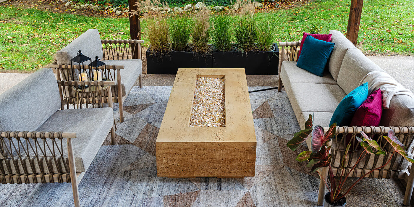 A covered outdoor patio space with seating an FlameCraft's Tuscan Gas Fire Pit, featuring a hand-stained Travertine finish