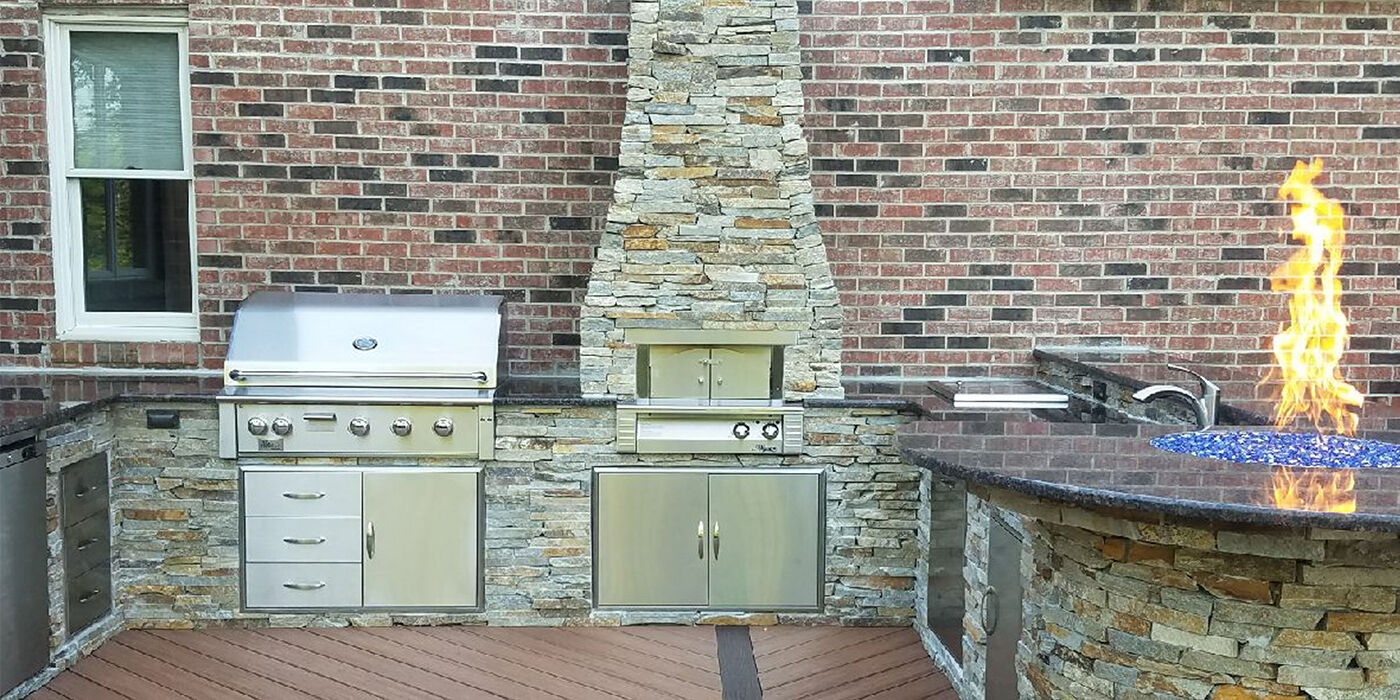 A large outdoor kitchen island with a grill, oven, storage doors, a bar area with seating, and a fire pit