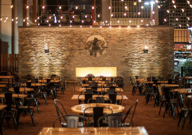 Outdoor patio with tables and chairs in front of a large stone wall with a fireplace in the middle