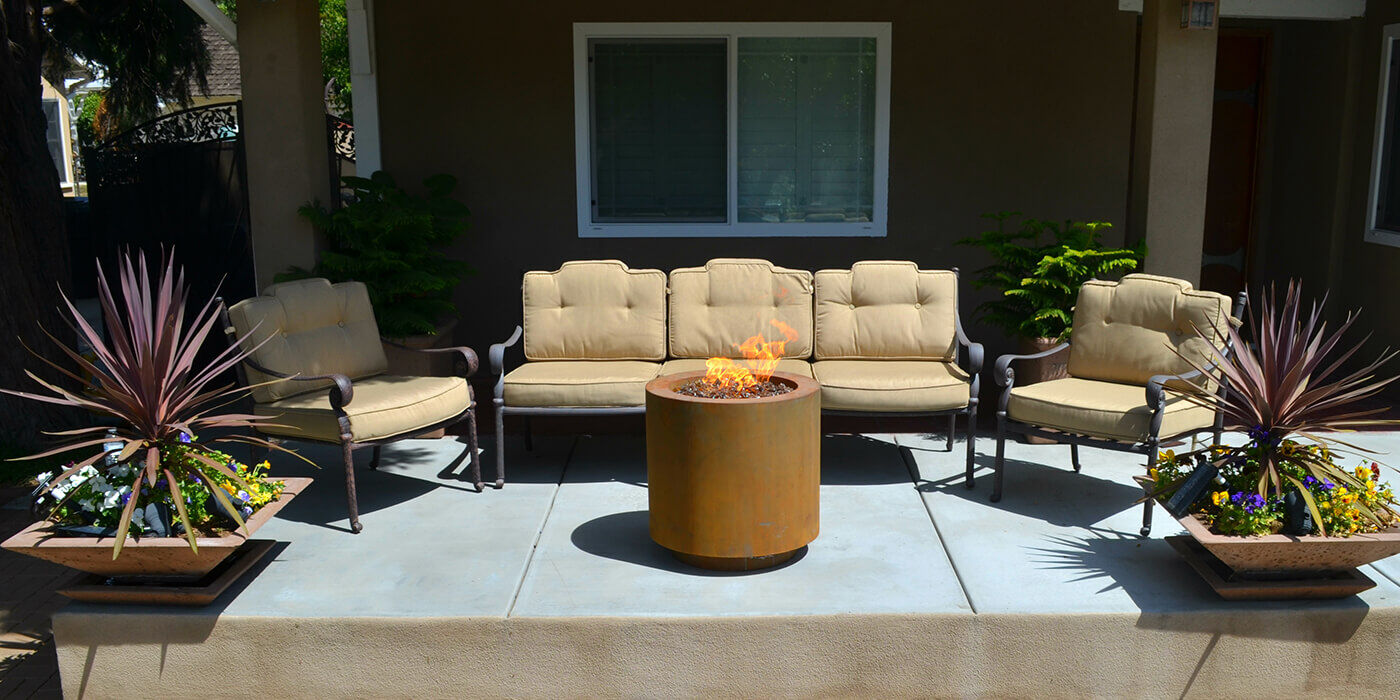 An outdoor patio space with a small, round Corten steel gas fire pit