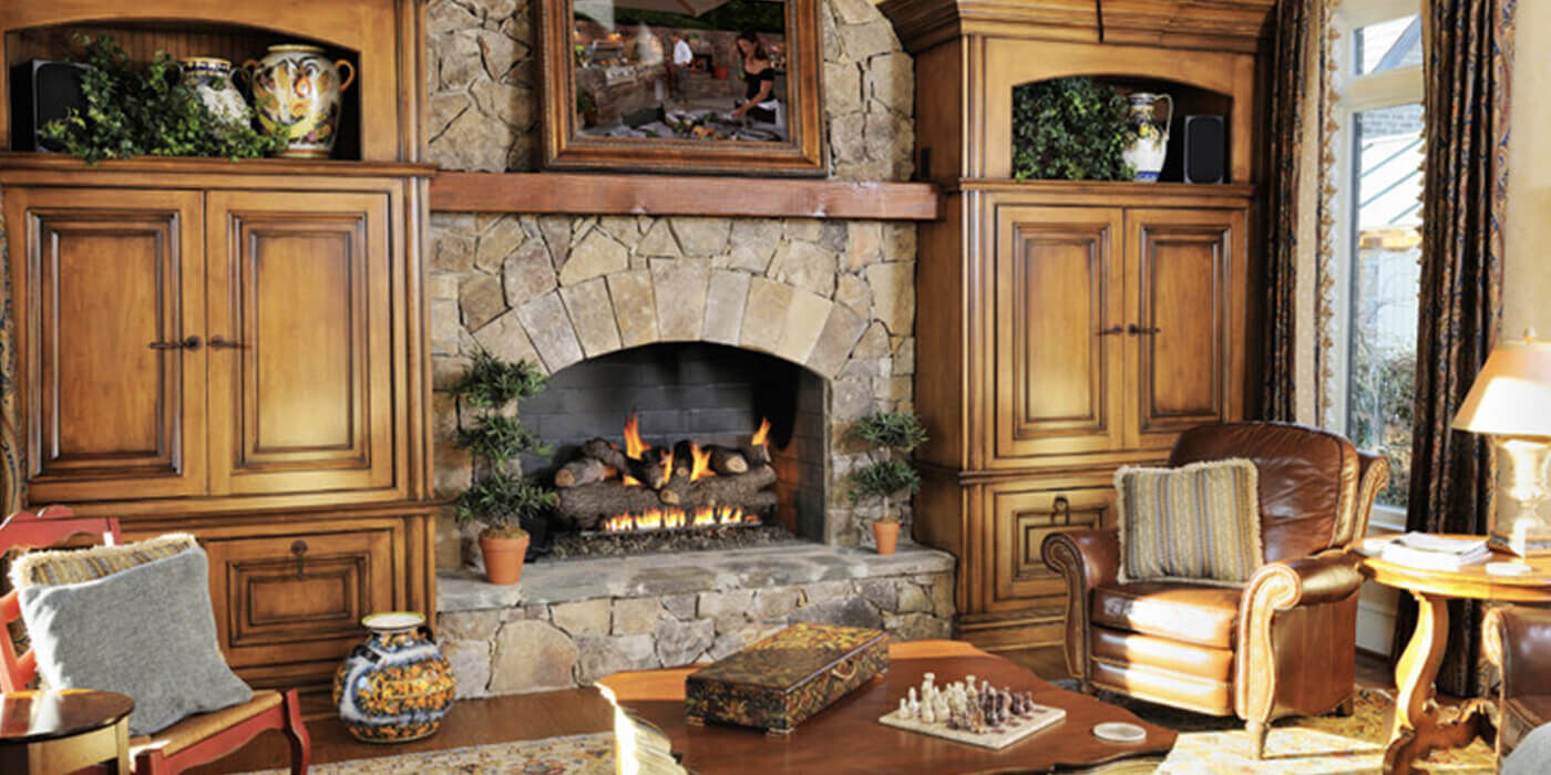 A rustic traditional living room with an arched gas fireplace and a large, charred gas log set