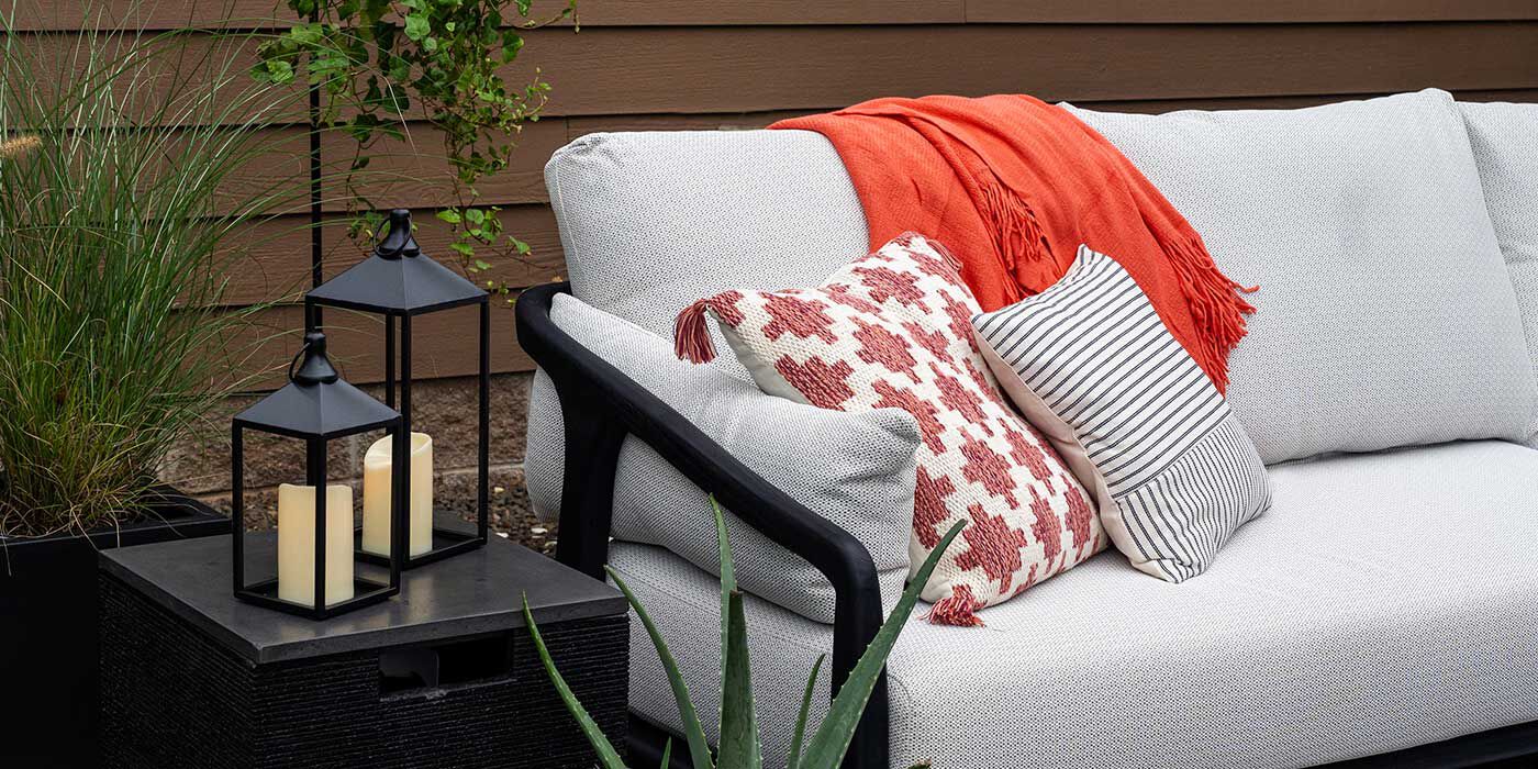 A white outdoor sectional sofa with an orange throw blanket, orange and white pillows, and a black frame