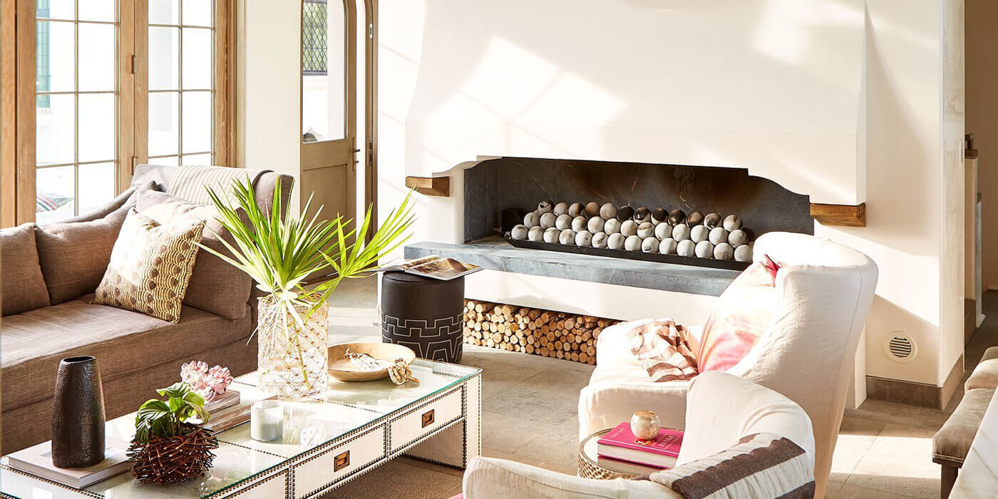 A Bohemian inspired living space with a large, linear gas fireplace and concrete fire balls 