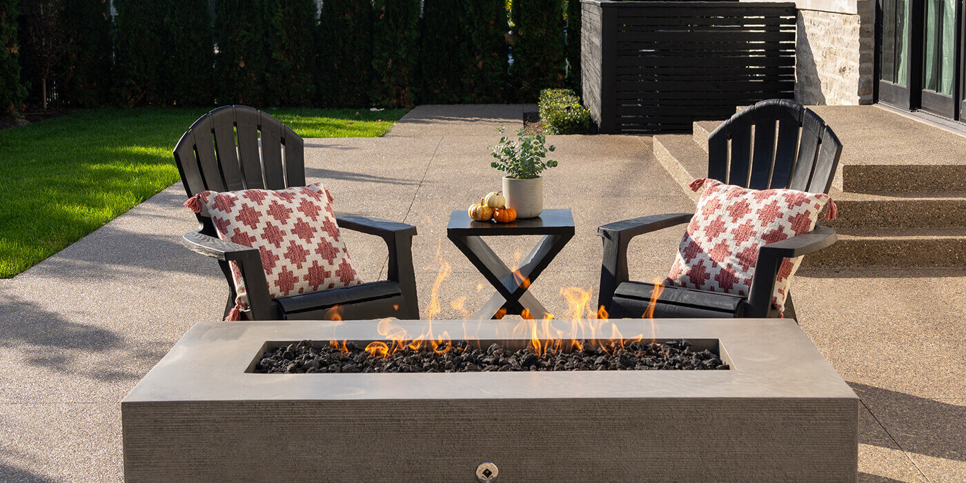 A linear gas fire pit with two chairs and a side table