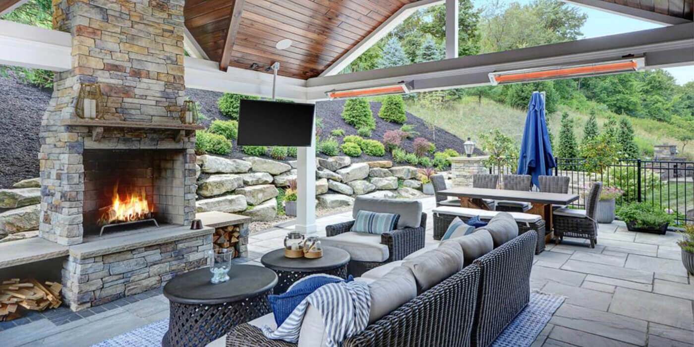 An outdoor living room with a large seating area and fireplace, a dining area, and two mounted patio heaters