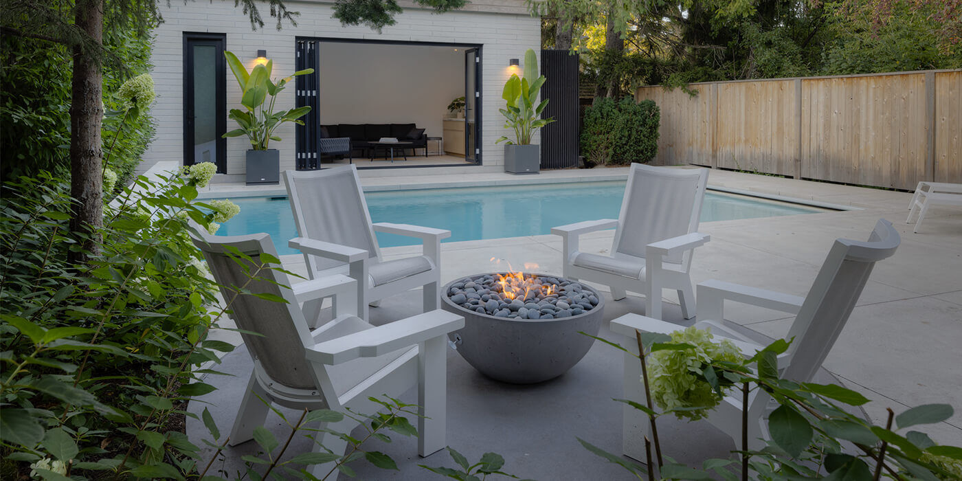 An outdoor sitting area near a with four chairs and a small gas fire bowl with a round fire pit burner