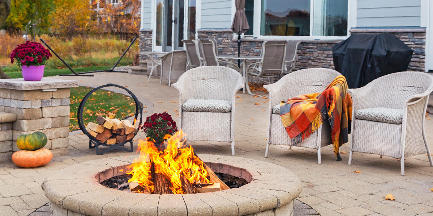 A backyard space with a built-in stone wood fire pit and chairs set up around it