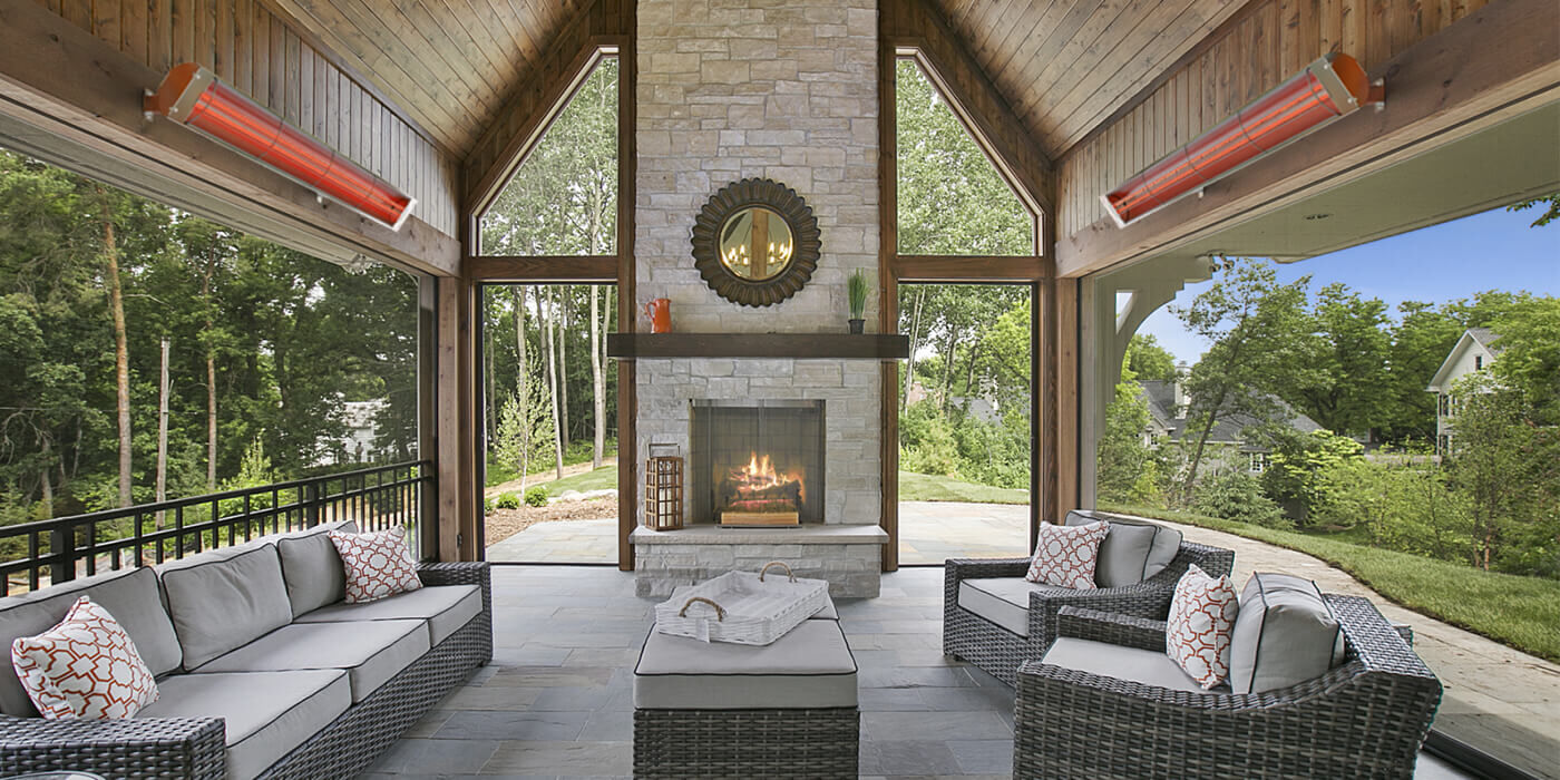 A covered outdoor living room with a fireplace and two mounted patio heaters
