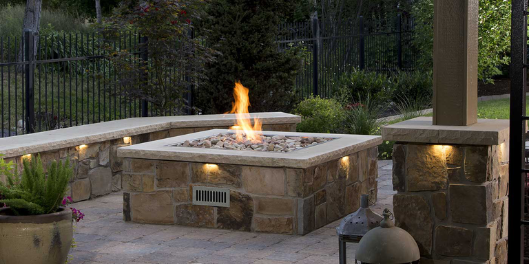 A large, square custom-built gas fire pit made of natural stone and concrete