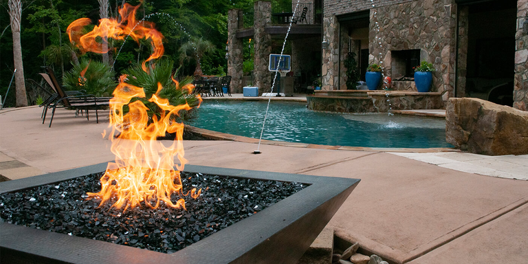 A gas fire pit with an HPC Fire burner system installed on an outdoor patio near a pool